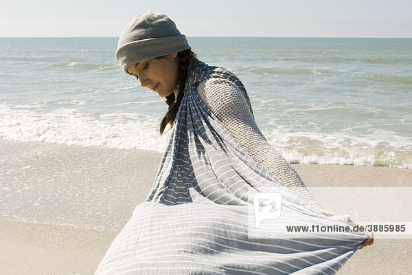 Teenagermädchen geht am Strand spazieren  hält einen Schal im Wind.