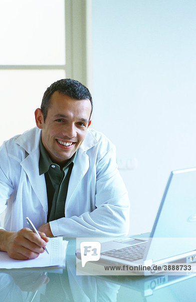 Arzt sitzend mit Laptop  Schreiben mit Stift auf Papier  Smiliing