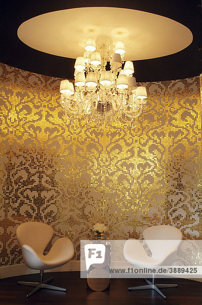 Mit kleinen Mosaiksteinen dekorierte Wand im exklusiven Wohnbereich mit luxuriöser Deckenlampe und zwei italienischen Designersesseln
