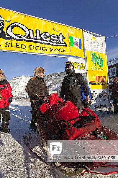 Dog musher Normand Casavant standing with his loaded sled  talking to race marshal Hans Oettli after arriving in Dawson City  Yukon Quest 1  000-mile International Sled Dog Race 2010  Yukon Territory  Canada
