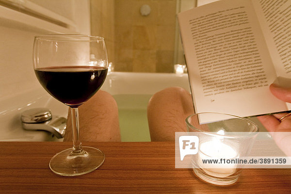 Man sitting in a bathtub  bathing  reading a book  drinking wine  candles  spa  relaxing