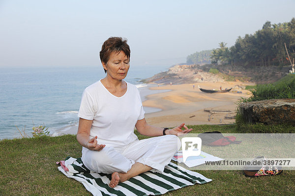Frau meditiert auf Wiese über Meer  Bethsaida Hermitage bei Kovalam  Kerala  Südindien  Indien  Asien