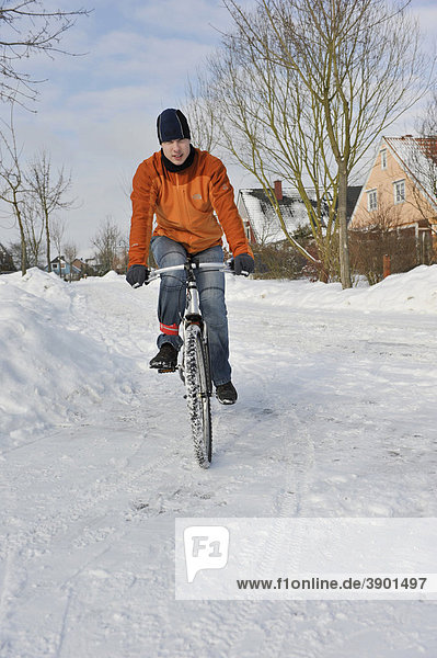 Jugendlicher fährt mit dem Fahrrad auf winterlicher verschneiter Straße