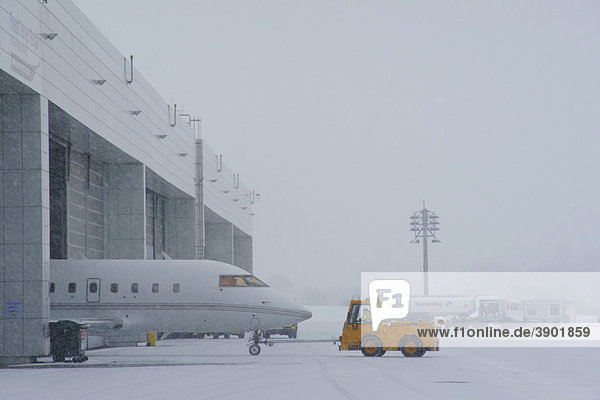 Snow  winter  towtruck pulling an aircraft  Hangar  General Aviation  GAT  east apron  Munich Airport  MUC  Bavaria  Germany  Europe