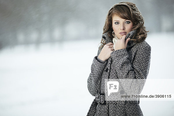 Portrait einer jungen Frau im Schnee  ihre Hand den Mantelkragen haltend