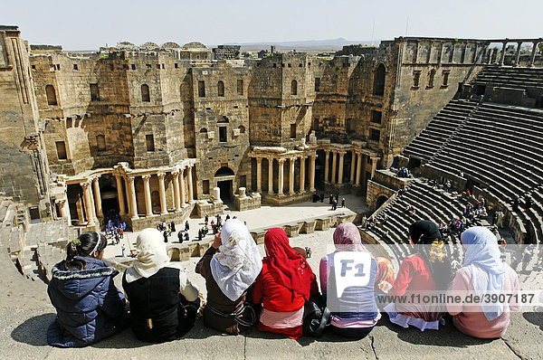 Mädchen mit Kopftuch sitzen auf einer Stufe der Treppe im Zuschauerraum  römisches Theater in Bosra  Syrien  Asien