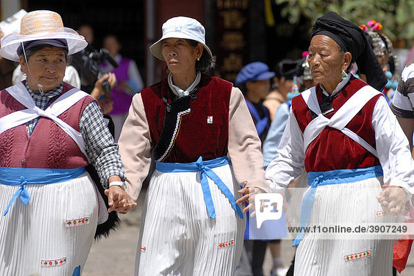 Three women in traditional costume of the Naxi minority holding hands and dancing on the main square in Lijiang  Yunnan  Southwest China  Asia