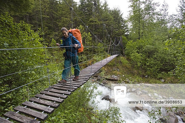 Frau  Wanderin mit Rucksack überquert die Hängebrücke über den Taja River Fluß  nahe der historischen Canyon City  pazifischer Nordwesten  Küsten-Regenwald  Chilkoot Trail Wanderweg  Chilkoot Pass  Alaska  USA
