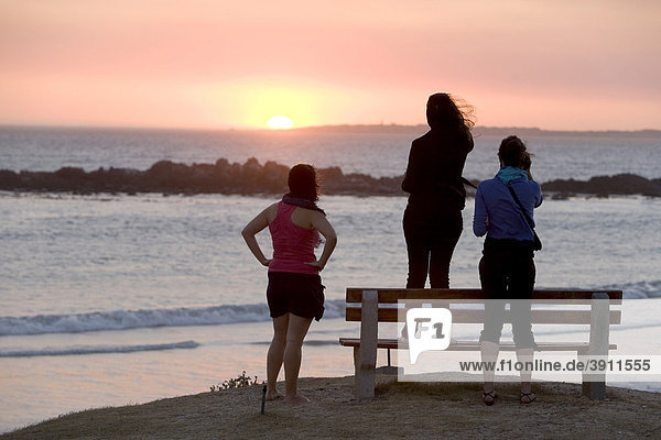 Drei Mädchen betrachten den Sonnenuntergang am Bloubergstrand bei Kapstadt  Westkap  Südafrika  Afrika