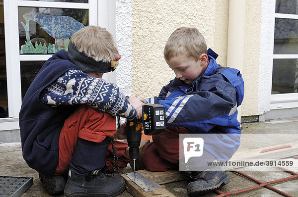Two small boys  7 and 9  screwing a screw into a wooden frame with a cordless screwdriver