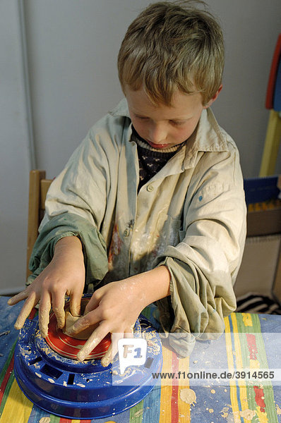 Kleiner Junge  7 Jahre  töpfert an einer Drehscheibe ein Gefäß aus Ton