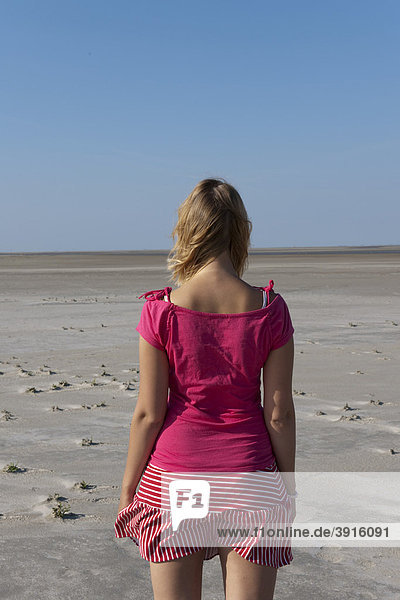 Junge Frau  20-25 Jahre  steht am weiten Sandstrand von St Peter Ording und blickt in die Ferne  Nordsee  Nordfriesland  Schleswig-Holstein  Norddeutschland  Deutschland  Europa