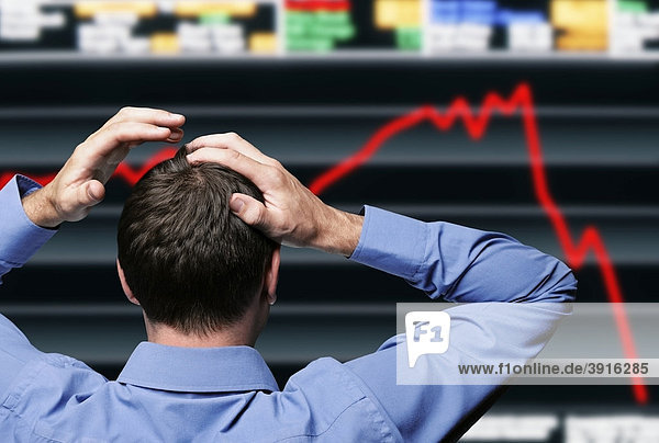 Börsenmakler vor einer Anzeigetafel die einen Börsencrash zeigt fasst sich an den Kopf