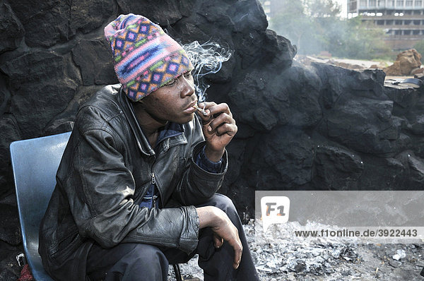 Obdachloser Immigrant aus Mosambik konsumiert Drogen  Marihuana  und wärmt sich am frühen Morgen an einem Feuer im Park Pullinger Kop  Stadtteil Hillbrow  sozialer Brennpunkt im Zentrum von Johannesbug  Südafrika  Afrika