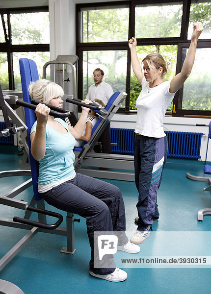 Patientin beim Muskelaufbautraining an verschiedenen Kraftmaschinen im Trainingsraum  Physiotherapie in einem neurologischen Rehabilitationszentrum  Bonn  Nordrhein-Westfalen  Deutschland  Europa