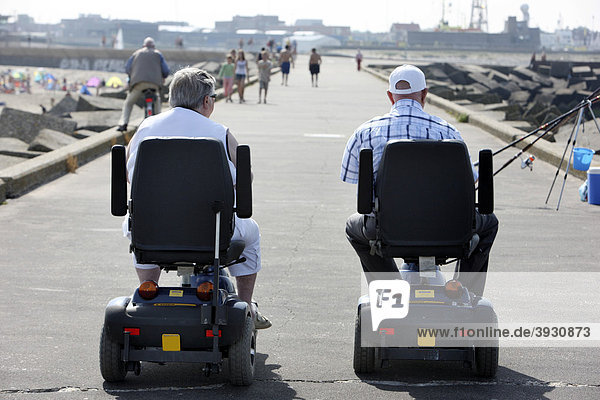 Senior citizens on motorized wheelchairs on a concrete breakwater on the beach of Scheveningen  beach district of The Hague  the largest seaside resort in the Netherlands  Europe