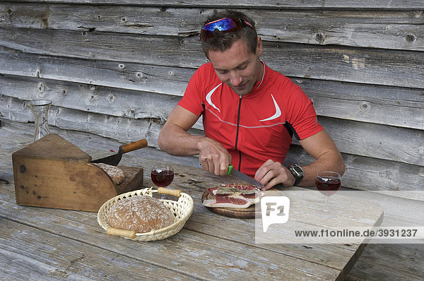 Bicycle racer cutting South Tyrolean bacon at the mountain lodge on the Passo di Pennes  South Tyrol  Italy  Europe