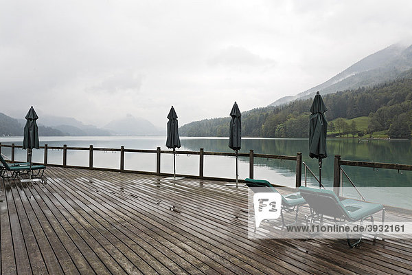 Terrasse mit geschlossenen Sonnenschirmen und Liegen am See  bedeckter Himmel  Regenwetter  triste Stimmung  Fuschlsee  Salzkammergut  Salzburger Land  Salzburg  Österreich  Europa