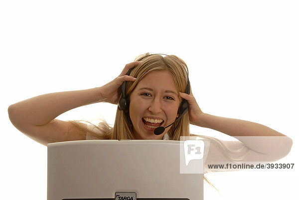 Achtzehnjährige Frau hinter Laptop mit Headset lachend  sich die Haare raufend
