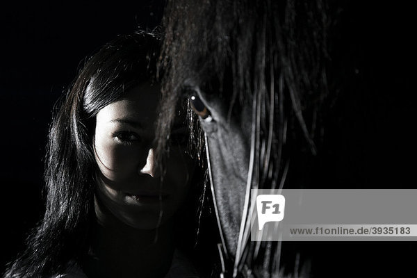 Junge Frau steht neben ihrem dunkelbraunen Pferd  direkter Blick