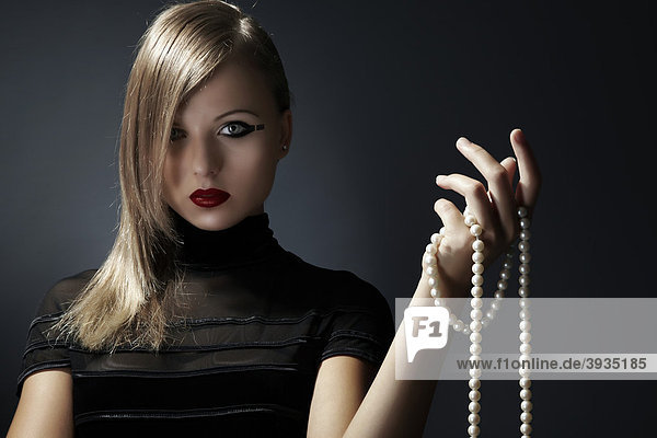 Jungen blonde Frau im schwarzen Kleid hält eine Perlenkette in ihrer Hand  Fashion