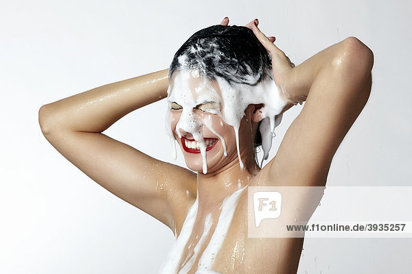 Fröhliche junge Frau mit Schaum in ihrem Haar beim Duschen
