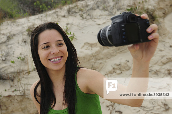 Frau mit digitaler Spiegelreflexkamera macht ein Selbstportrait am Strand