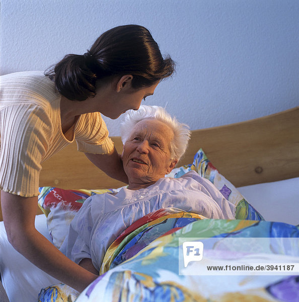 Eine Altenpflegerin betreut eine im Bett liegende Senioren
