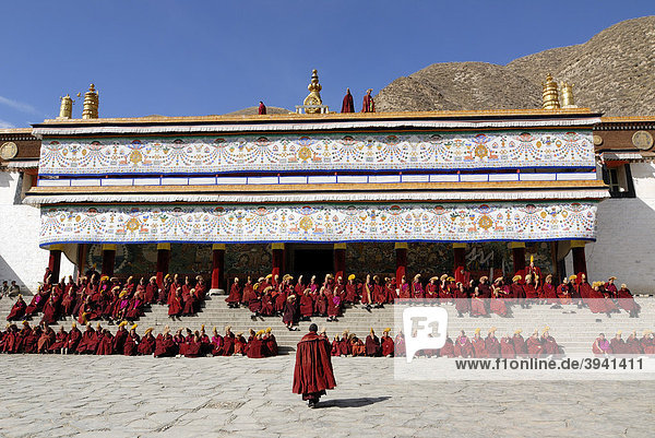 Tibetische Mönche in Mönchsrobe des Gelukpaordens sitzen auf den Treppen vor der Versammlungshalle  tibetisch Dukhang  des Kloster Labrang  Xiahe  Gansu  China  Asien