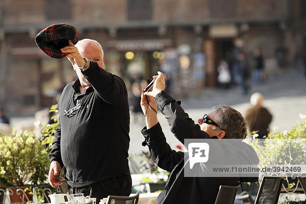 Mann schirmt Kamera mit Mütze vor der Sonne ab während Frau fotografiert  Siena  Toskana  Italien  Europa