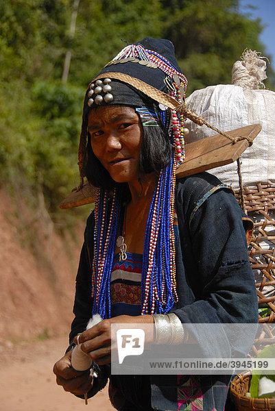 Armut  Portrait  Frau der Akha Djepia Ethnie  traditionelle bunte Kleidung  Haube als Kopfbedeckung  Spinnen von Baumwolle zum Faden  Tragen einer Last über Joch auf den Schultern  Ban Khay  Distrikt Boun Tai  Provinz Phongsali  Laos  Südostasien  Asien