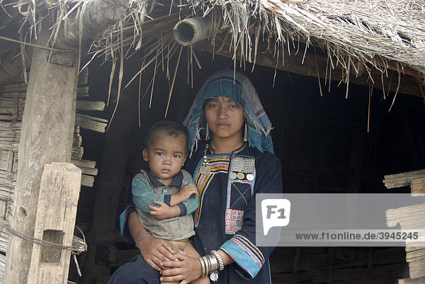 Armut  junge Frau der Akha Nuqui Ethnie  Kleinkind auf dem Schoß  Tracht  traditionelle Kleidung  Farbe Indigo  Kopfbedeckung Tuch  vor Hütte  Dorf Ban Phou Yot  Provinz und Distrikt Phongsali  Laos  Südostasien  Asien