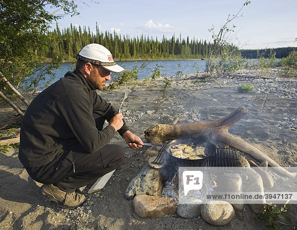 Ein Mann brät Fischfilets in einer Pfanne auf einem Lagerfeuer  Kessel  oberer Liard River  Yukon Territory  Kanada