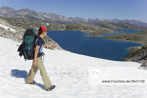 Young woman  hiker with backpack  hiking in snowfield  panorama near summit of historic Chilkoot Pass  Chilkoot Trail  Crater Lake behind  alpine tundra  Yukon Territory  British Columbia  B. C.  Canada