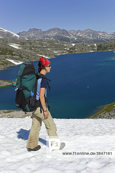 Young woman  hiker with backpack  hiking in snowfield  panorama near summit of historic Chilkoot Pass  Chilkoot Trail  Crater Lake behind  alpine tundra  Yukon Territory  British Columbia  B. C.  Canada