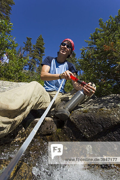 Junge Wanderin filtert frisches Trinkwasser aus einem Bach  Filterung  Schutz vor Giardien  historischer Chilkoot Pass  Chilkoot Trail Wanderweg  Yukon Territory  British Columbia  BC  Kanada