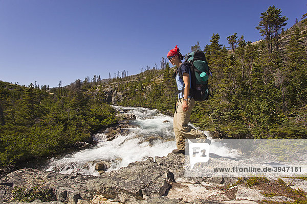 Young woman hiking  backpacking  hiker with backpack  historic Chilkoot Pass  Chilkoot Trail  Moose Creek Canyon waterfall behind  Yukon Territory  British Columbia  B. C.  Canada
