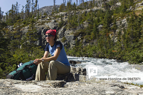Young woman  hiker  backpacker sitting on rock  resting  Moose Creek Canyon  waterfall behind  historic Chilkoot Pass  Chilkoot Trail  Yukon Territory  British Columbia  B. C.  Canada