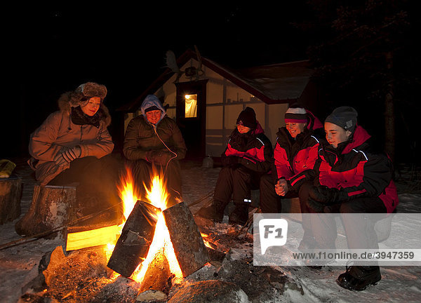 Menschen sitzen an einem Lagerfeuer  Feuer  dahinter beleuchtetes Hauszelt  Hütte  Yukon Territory  Kanada