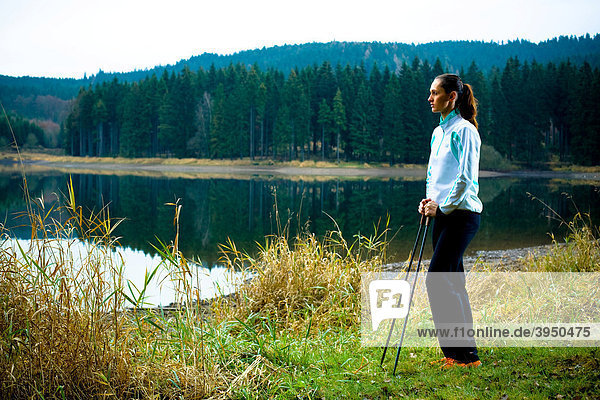 Junge Frau wandert am See im Nordic Walking Stil