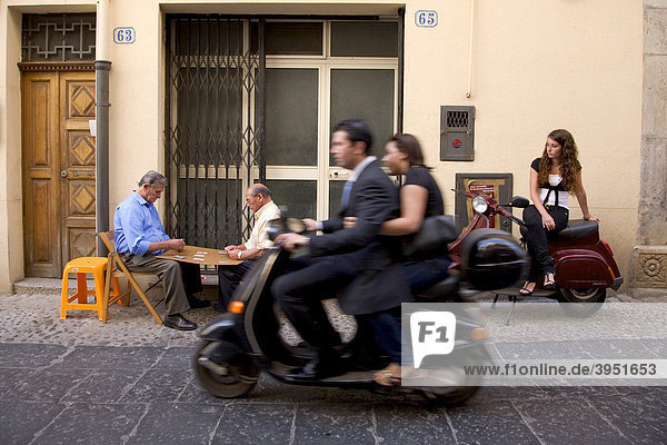 Street scene  men playing cards  girl sitting on a Vespa  Cefalu  Palermo Province  Sicily  Italy  Europe
