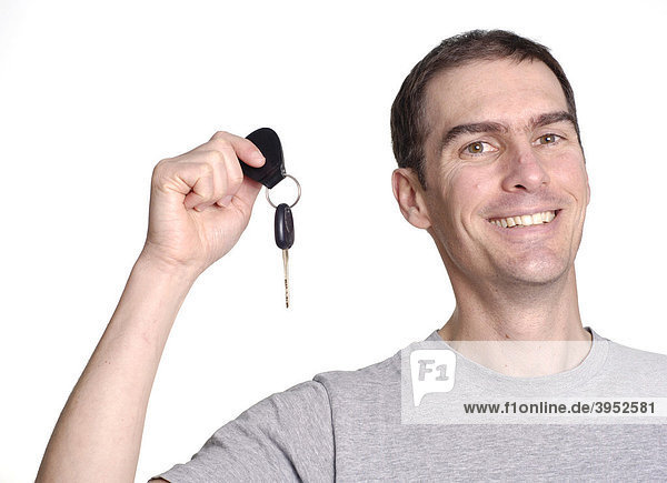 Lächelnder junger Mann hält einen neuen Autoschlüssel hoch