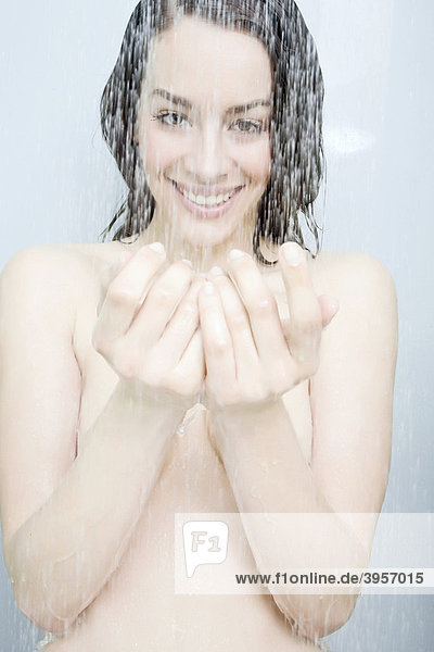 Junge Frau unter der Dusche lacht den Betrachter an