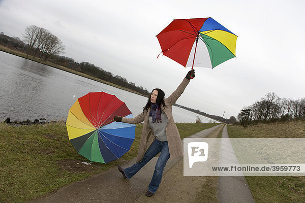Junge Frau  30-35 Jahre  mit bunten Regenschirmen  gibt am Nord-Ostsee-Kanal den vorbeifahrenden Schiffen Signalzeichen  Schleswig-Holstein  Deutschland  Europa