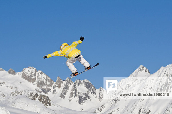 Skier jumping  against blue sky  snow-covered mountain chain in the back  Andermatt  Switzerland