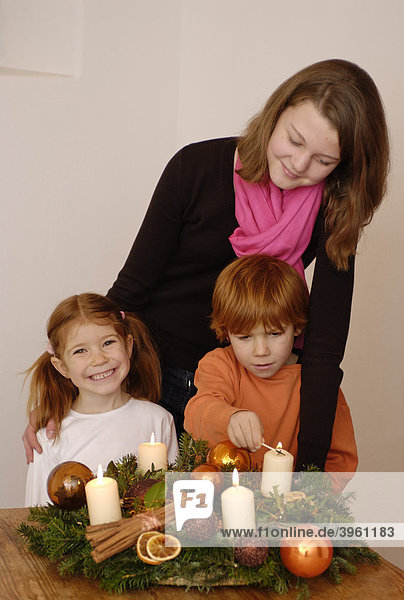 Junge Frau mit Kindern zündet Kerzen an einem Adventskranz an