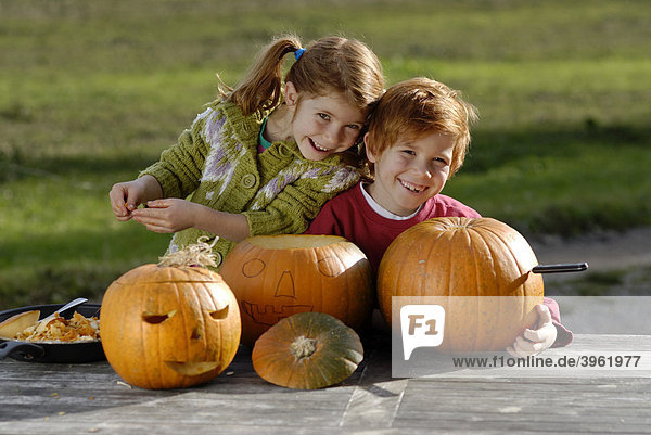 Zwei Kinder beim Kürbiskopf schnitzen für Halloween Herbstdekoration