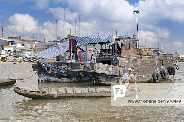 Man with a small rowboat in front of a merchant boat  market boat on the Mekong River  Mekong Delta  Vietnam  Asia