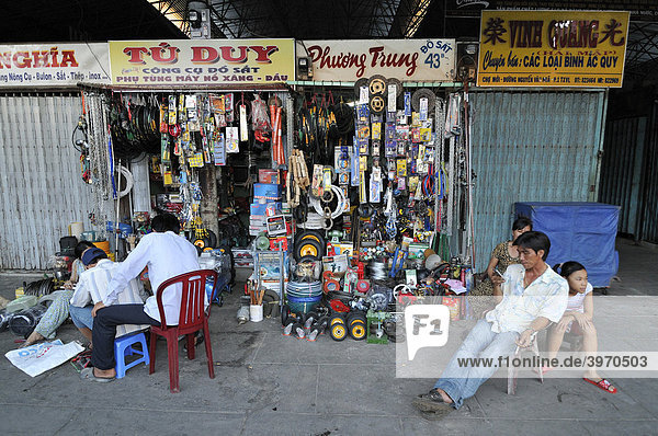 Family sitting in front of a shop on the market  iron and household store  man playing with mobile phone Vinh Longh  Mekong Delta  Vietnam  Asia
