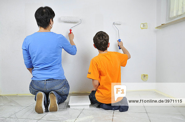 Malerarbeiten  Mutter und Sohn streichen Wand mit Farbrolle